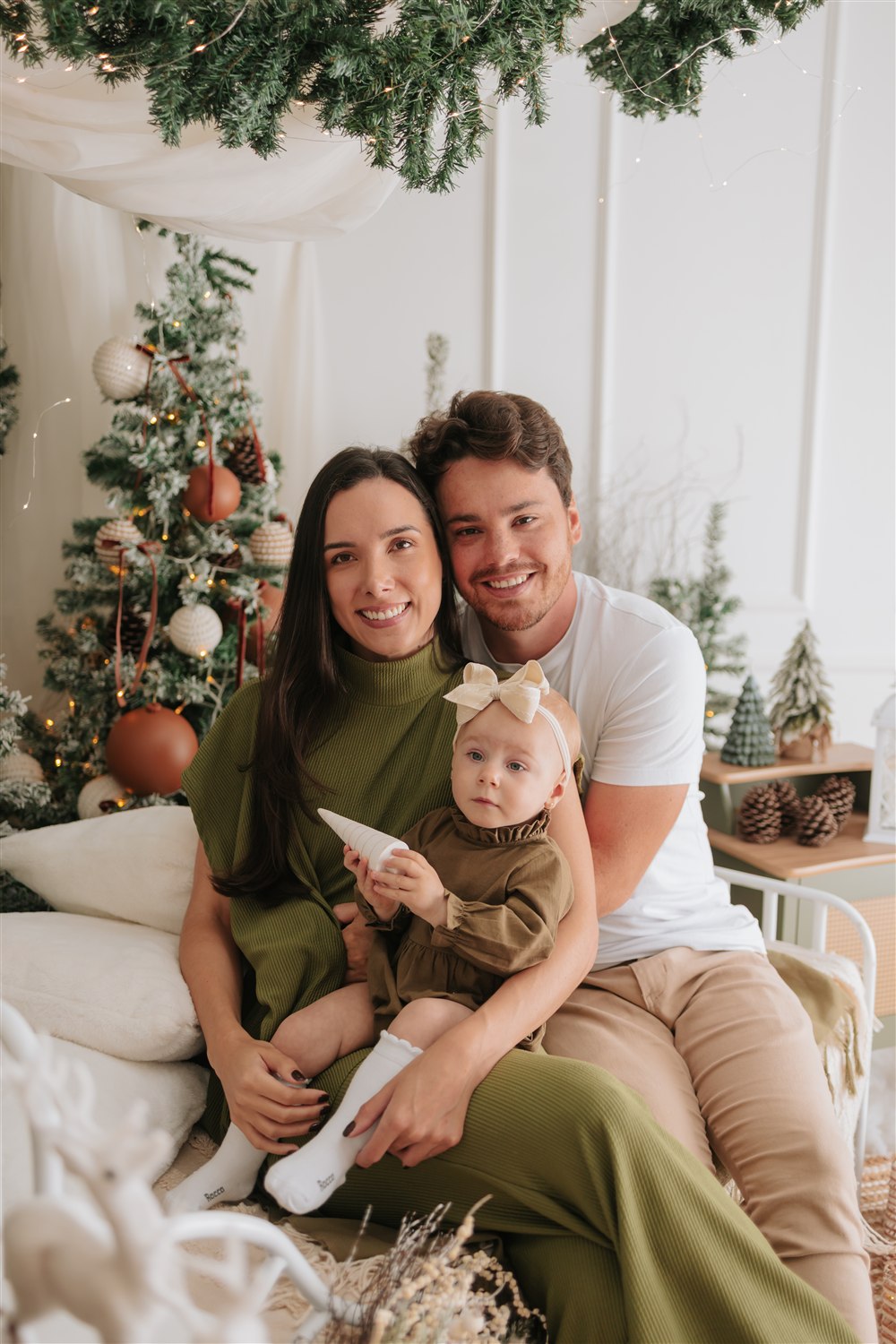 Mãe, pai e bebê abraçados em um cenário acolhedor de Natal